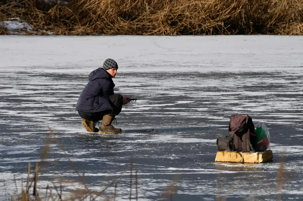 A guest enjoying ice fishing on a peaceful frozen lake wrapped in warm winter clothing
